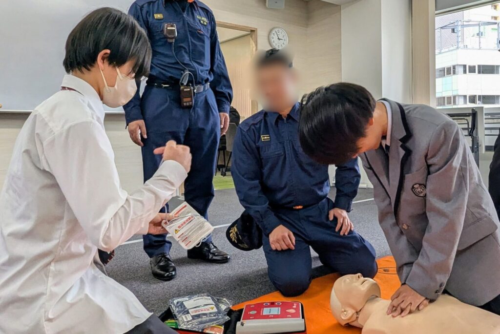 AEDのパッドを確認する生徒と、心臓マッサージをする生徒